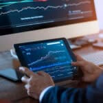 Businessman checking stock market on digital tablet and a desktop computer with stock exchange graph on screen. Financial stock market. Analyzing data in office background.